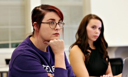 Two TCU graduate students laugh in a spirited exchange in their Communication Studies class