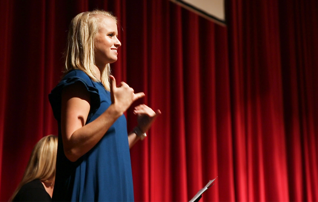 Female standing on stage, using sign language