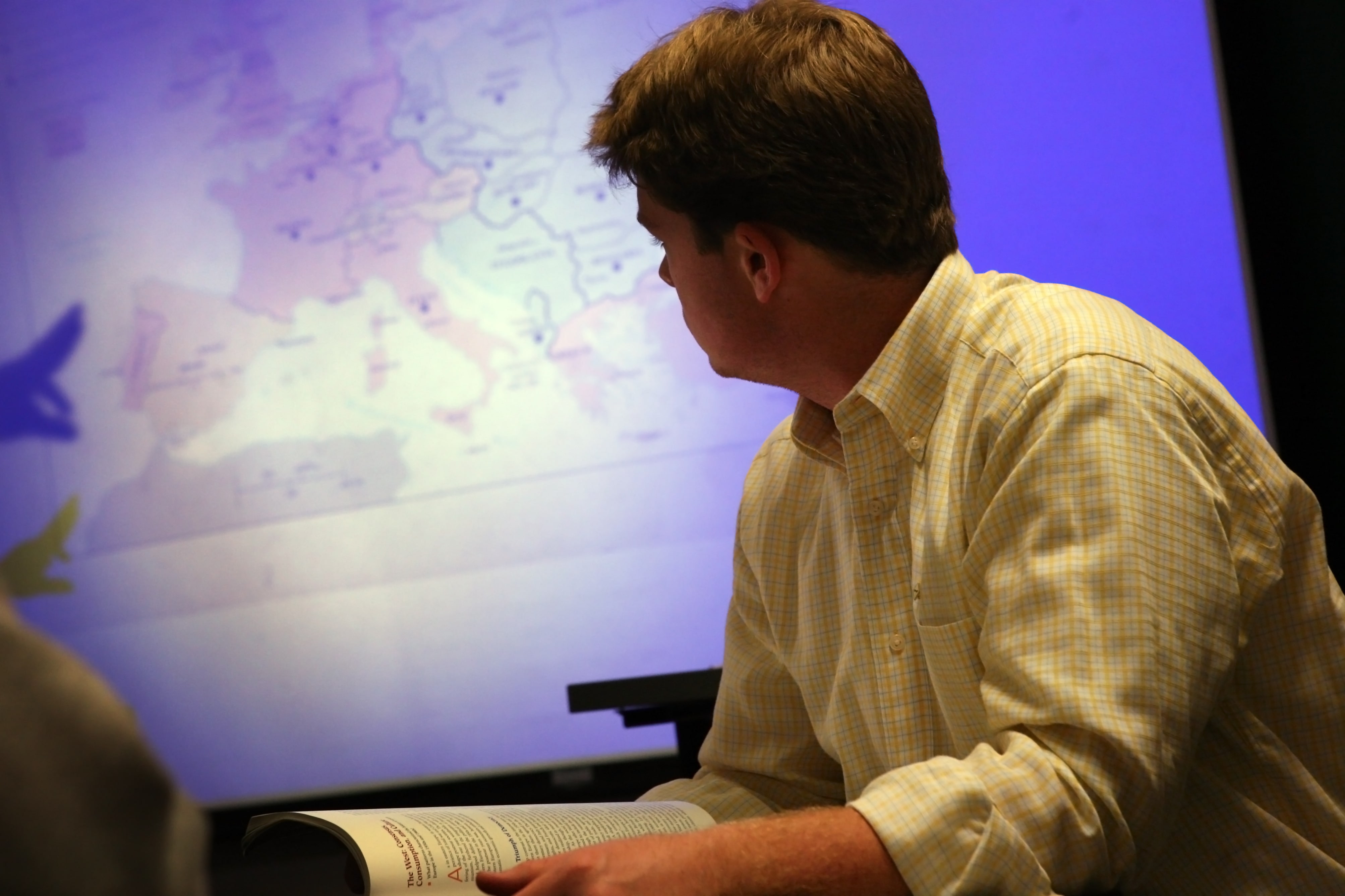 A student studies a map projected on a large screen in a classroom.