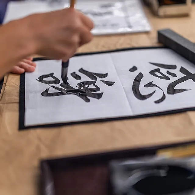 Person writing Japanese calligraphy on a large piece of paper