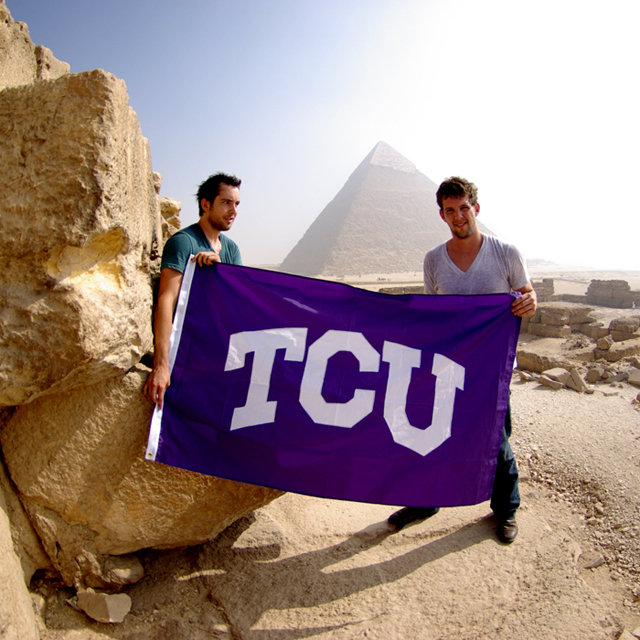 Two male students near pyramid with TCU flag