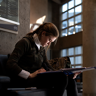 A young women sits alone and looks down intently at her book in the sunlit lobby of TCU's Moudy Hall North.