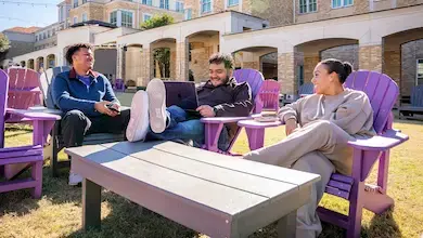 Three students sit in purple lounge chairs in the Campus Commons lawn area