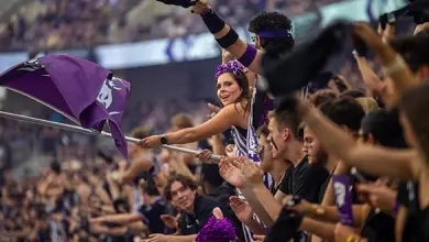 Female student waves a Horned Frog flag in a big group of TCU students while watching a football game